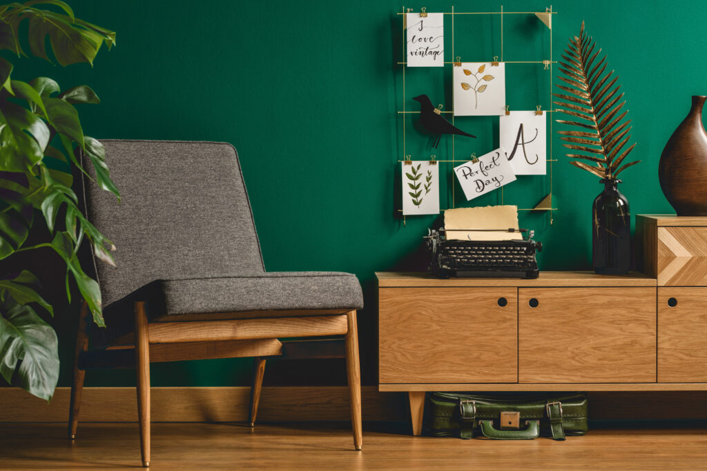 Grey armchair, wooden cupboard, typewriter and metal wall organizer in green living room interior